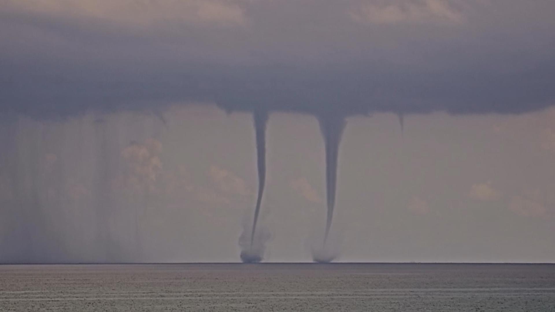 Stemming from a large dark cloud, the waterspouts can be seen moving closer together before one appears to dissipate.